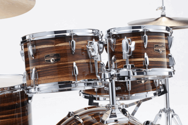 Detailansicht eines Tama Imperialstar IP50H6W-CTW Schlagzeugs mit braun-gestreifter Holzoptik und glänzenden Chrom-Beschlägen vor weißem Hintergrund.