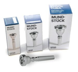 Ein silberfarbenes Gewa Cup 1 1/2 C Trompetenmundstück mit der Artikelnummer 710.002 liegt vor drei blauen und weißen Produktverpackungen desselben Modells auf einer weißen Oberfläche.