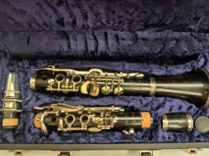 Eine gebrauchte, schwarze Hammerschmidt Es-Klarinette liegt zerlegt mit Zubehör in einem dunkelblauen Koffer.