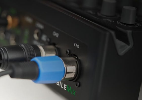 Nahaufnahme eines schwarzen DJ-Mischpults mit zwei eingesteckten Audio-Kabeln, wovon eines einen blauen Stecker hat.