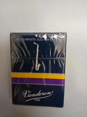 Eine dunkelblaue Verpackung mit der Aufschrift "Vandoren Paris" und "10 Clarinette Alto Mib-Eb 1 1/2", verziert mit einem weißen Saxophonsymbol und horizontalen Streifen in Gelb und Lila, liegt auf einem hellen Untergrund.