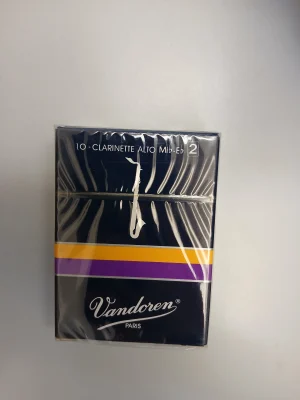 Eine dunkelblaue, rechteckige Verpackung für Vandoren Alt-Klarinettenblätter der Stärke 2 mit der Aufschrift "Vandoren PARIS" in Weiß und einem lilafarbenen sowie einem gelben Streifen ist zu sehen, die in transparenter Plastikfolie eingeschweißt ist.