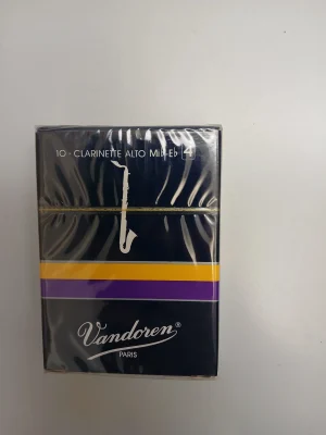 Eine rechteckige, dunkelblaue Packung Vandoren Alt-Klarinettenblätter der Stärke 4 mit gelben und violetten Streifen liegt auf einem weißen Untergrund.