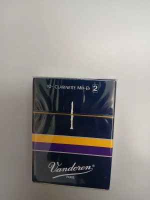 Eine dunkelblaue Schachtel Vandoren Es-Klarinette Classic / Traditional Stärke 2 (10 Stk.) liegt auf einem grauen Hintergrund.