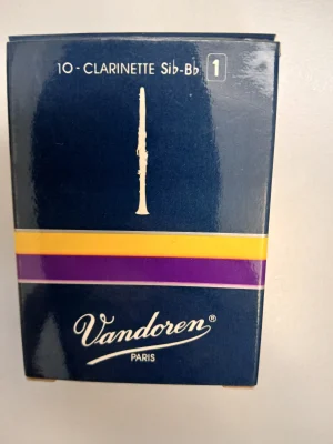 Eine dunkelblaue Schachtel „Vandoren Paris“ für 10 Klarinettenblätter der Stärke 1 mit einer Abbildung einer Klarinette und gelben sowie lilafarbenen Akzentstreifen ist vor einem hellen Hintergrund zu sehen.
