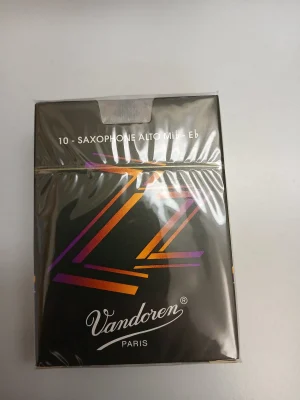 Die Abbildung zeigt eine verpackte, schwarze Schachtel "Vandoren Altsax Jazz Stärke 4 (10 Stk.)" mit einem abstrakten Z-Muster in Orange, Gelb und Lila auf der Vorderseite.