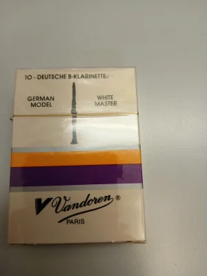 Die Abbildung zeigt eine Packung Vandoren B-Klarinettenblätter White Master German Classic/Traditional Stärke 4.5 (10 Stück) mit einem Bild einer Klarinette und den Farben Weiß, Gelb, Lila und Schwarz.