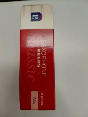 Eine rote Schachtel von Peter Leuthner Altsaxophonblättern Classic Vienna in Stärke 2,5 steht aufrecht und zeigt die Aufschrift "SAXOPHONE REEDS Classic" sowie ein Logo mit blauem Hintergrund und rotem Akzent.