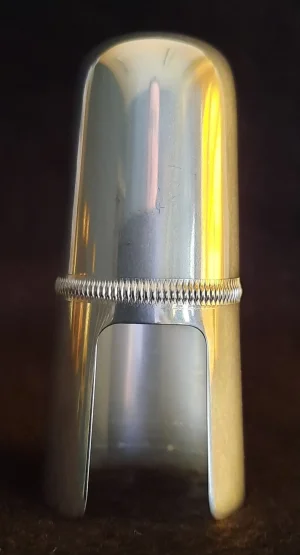 Eine silberne Kapsel für eine B-Klarinette mit einem gerippten Ring in der Mitte steht auf einer dunklen Oberfläche.