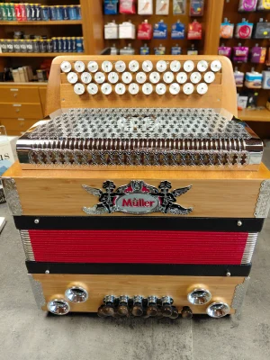 Eine gebrauchte, helle, hölzerne, dreireihige Steirische Harmonika der Marke Müller mit rotem Balg und silberfarbenen Beschlägen steht auf einem Tisch.