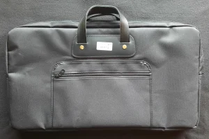 Eine schwarze Zithertasche Lenz 10654036 liegt horizontal und hat einen schwarzen Tragegriff sowie ein aufgenähtes Fach mit Reißverschluss.