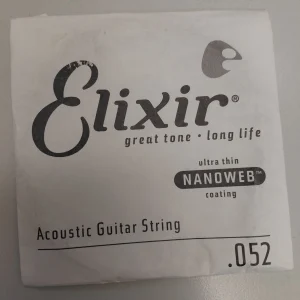 Eine quadratische, weiße Verpackung mit dem schwarzen Schriftzug "Elixir great tone long life", dem Hinweis "ultra thin NANOWEB coating", der Bezeichnung "Acoustic Guitar String" und der Angabe ".052" für eine einzelne E-Saite für Akustikgitarre mit Nanoweb-Beschichtung, abgebildet auf einer grauen Oberfläche.