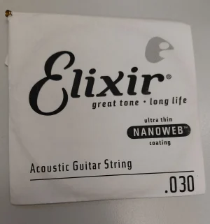 Die Nahaufnahme zeigt eine weiße Verpackung für eine einzelne Elixir Akustikgitarrensaite der Stärke .030 mit ultra dünner Nanoweb-Beschichtung und schwarzer Aufschrift.