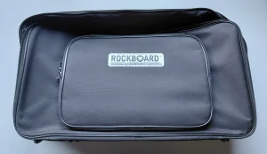 Eine offene, schwarze Rockboard Pedaltasche, mit einer aufgesetzten, rechteckigen Tasche und einem silbernen Rockboard-Logo, liegt flach auf einer hellen Oberfläche.