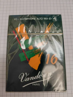 Eine dunkelblaue, noch eingeschweißte Packung Vandoren V16 Altsaxophonblätter der Stärke 4 liegt auf kariertem Papier.